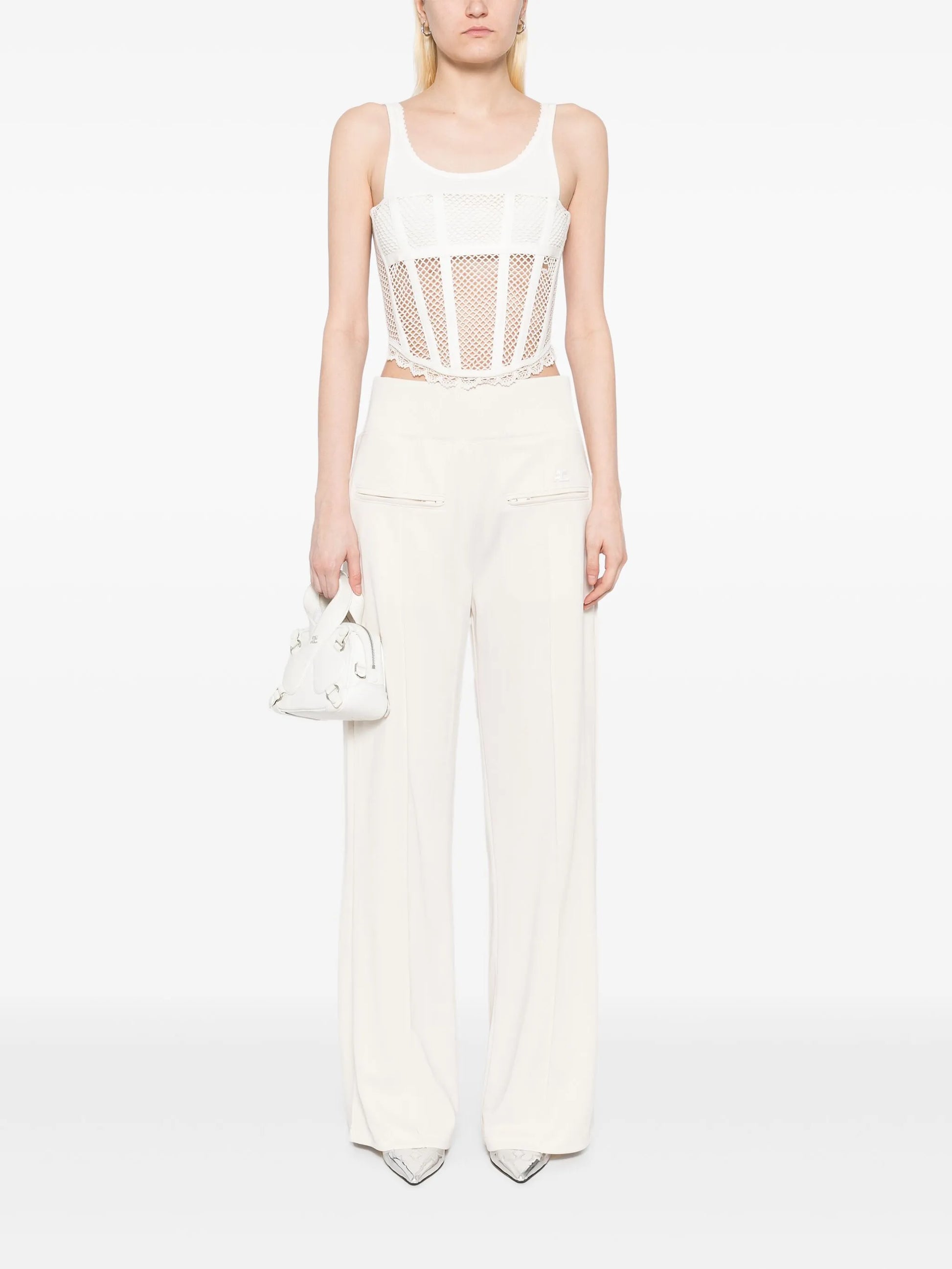 Person wearing a white sleeveless top with mesh design and matching pants on a white background