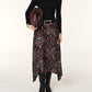 Woman wearing a black top and patterned skirt holding a brown leather bag on a white background