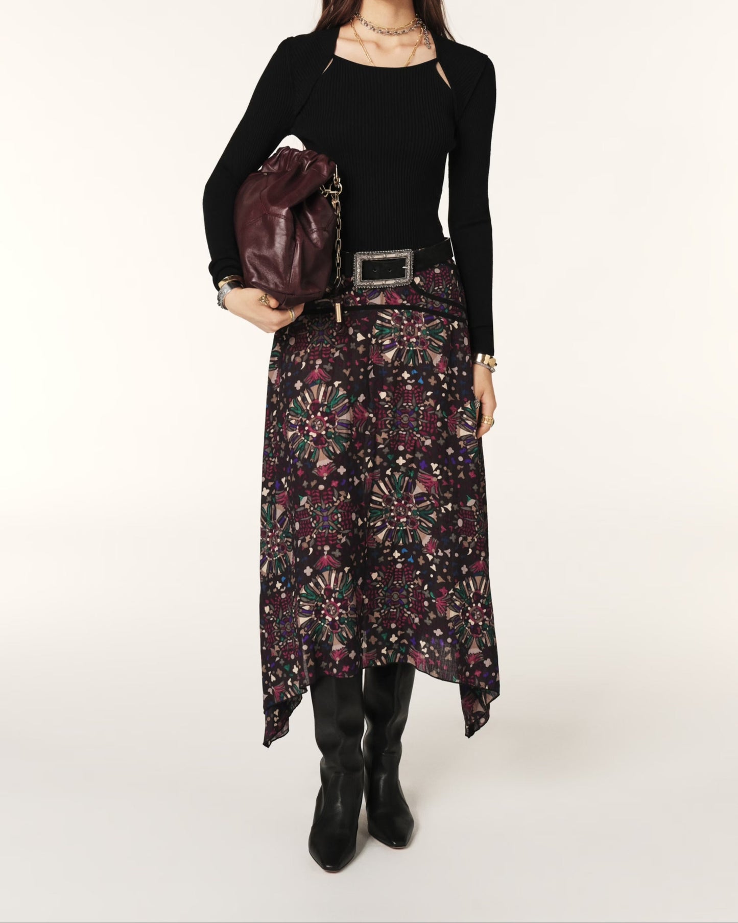 Woman wearing a black top and patterned skirt holding a brown leather bag on a white background