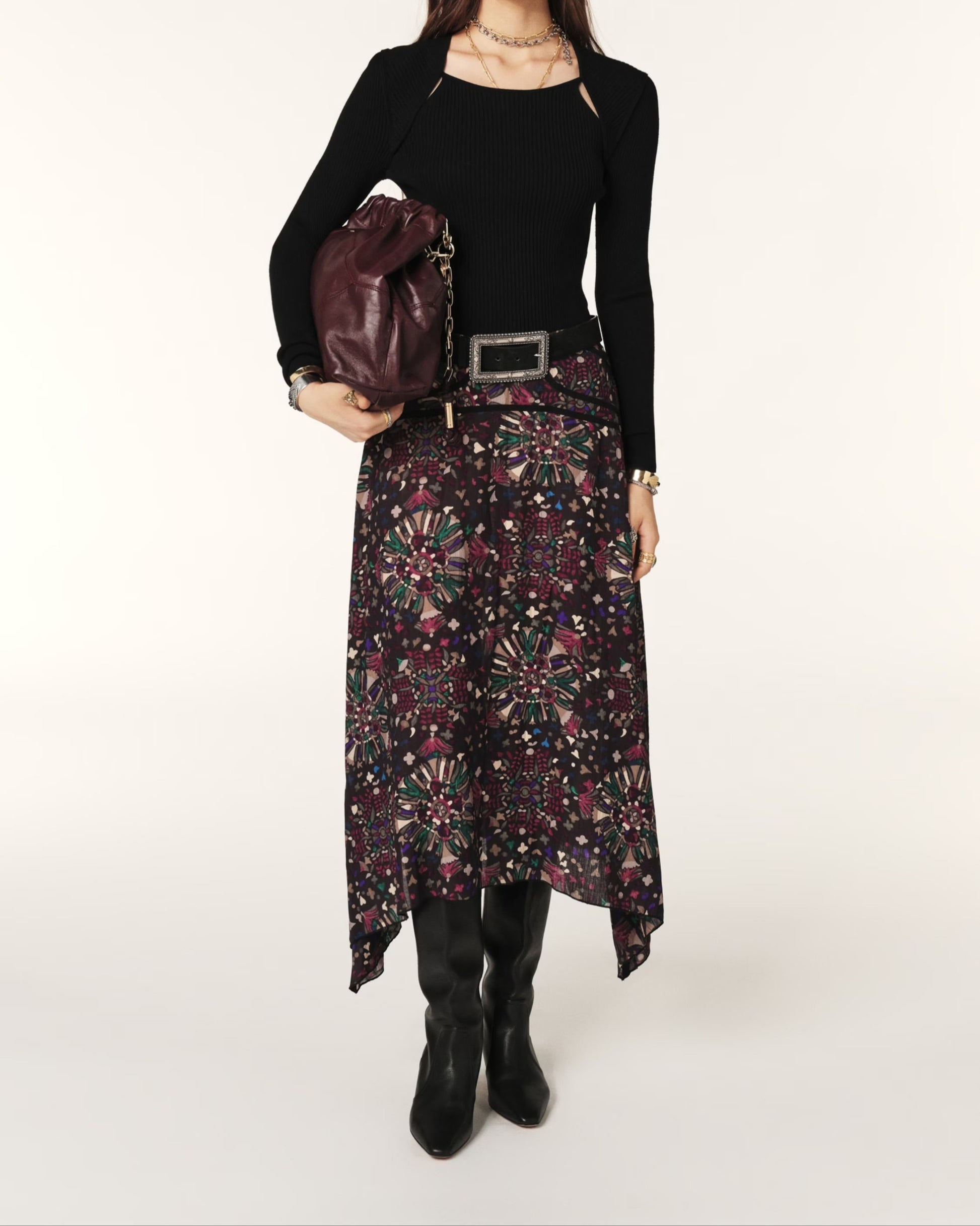 Woman wearing a black top and patterned skirt holding a brown leather bag on a white background