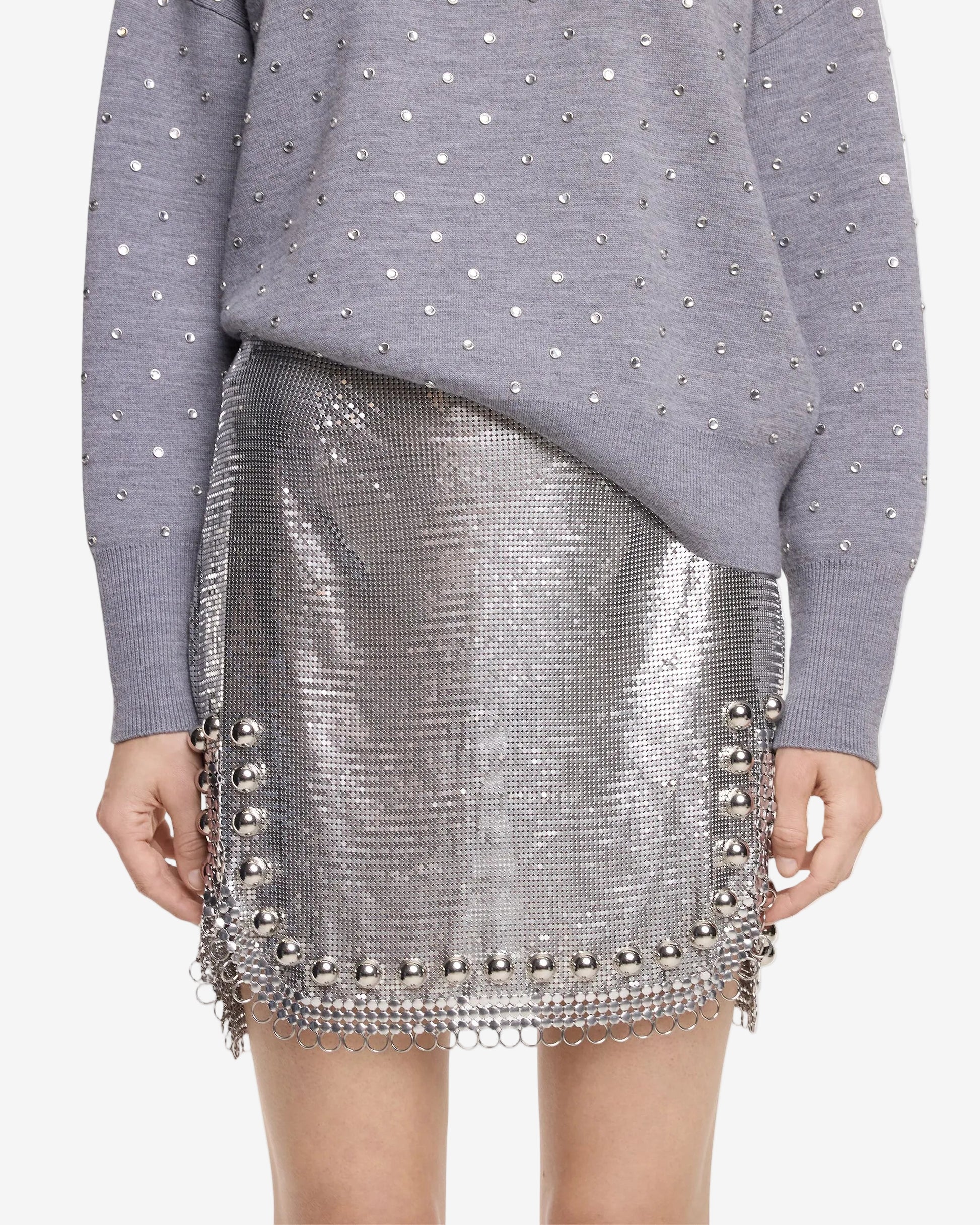 Person wearing a gray sweater with pearl embellishments and a silver sequin skirt on a white background