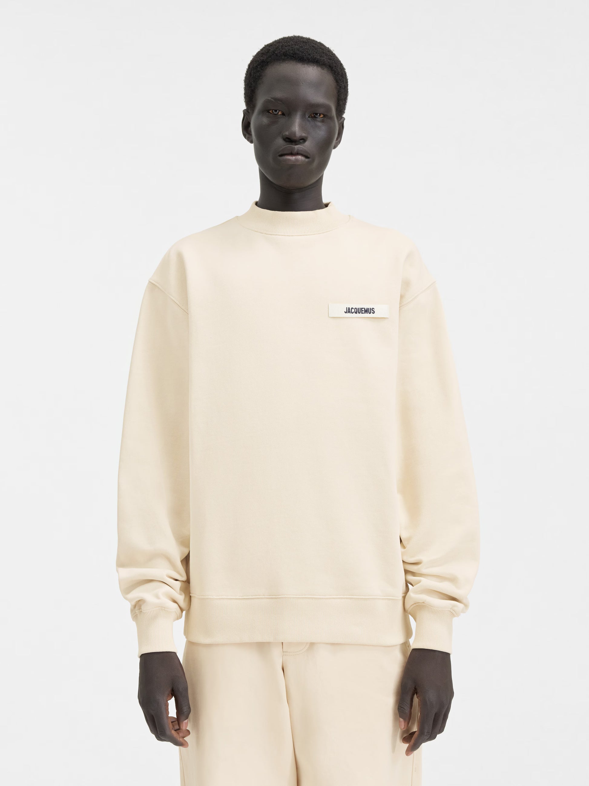 Person wearing a beige sweatshirt with a logo on a white background