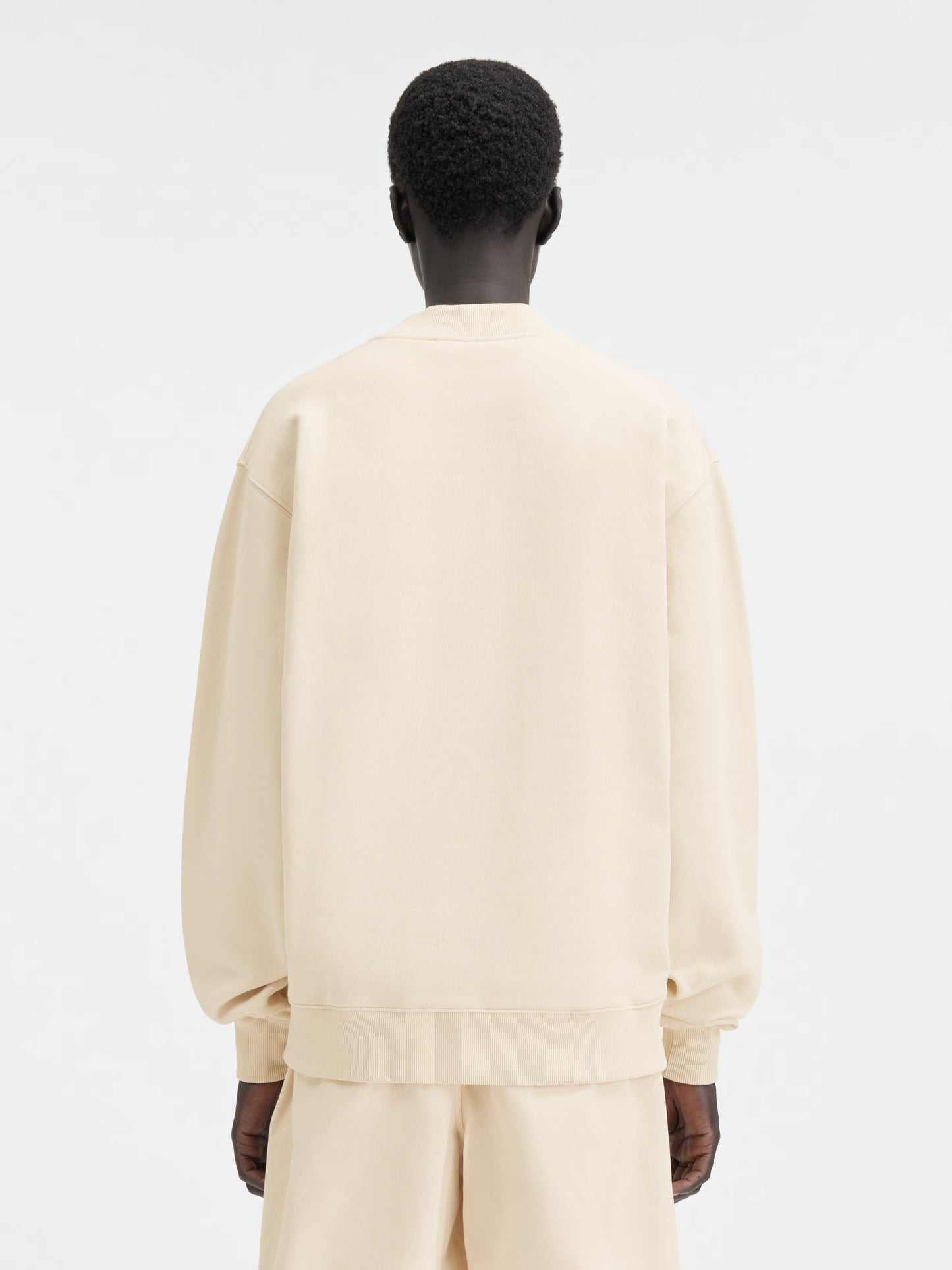 Person wearing a beige sweatshirt with a logo on a white background