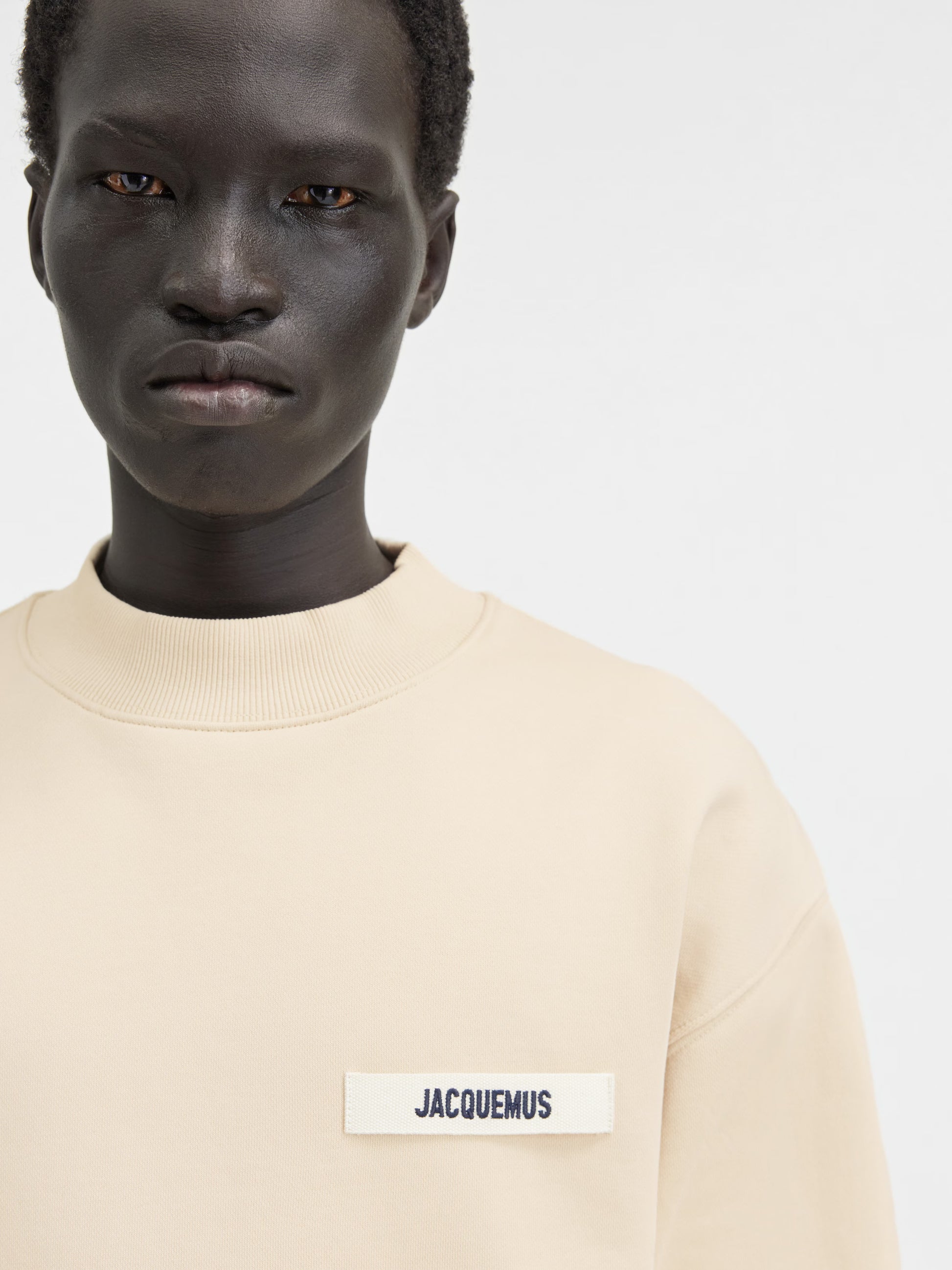 Person wearing a beige sweatshirt with a logo on a white background