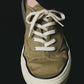 Green sneaker with white laces on a light beige background