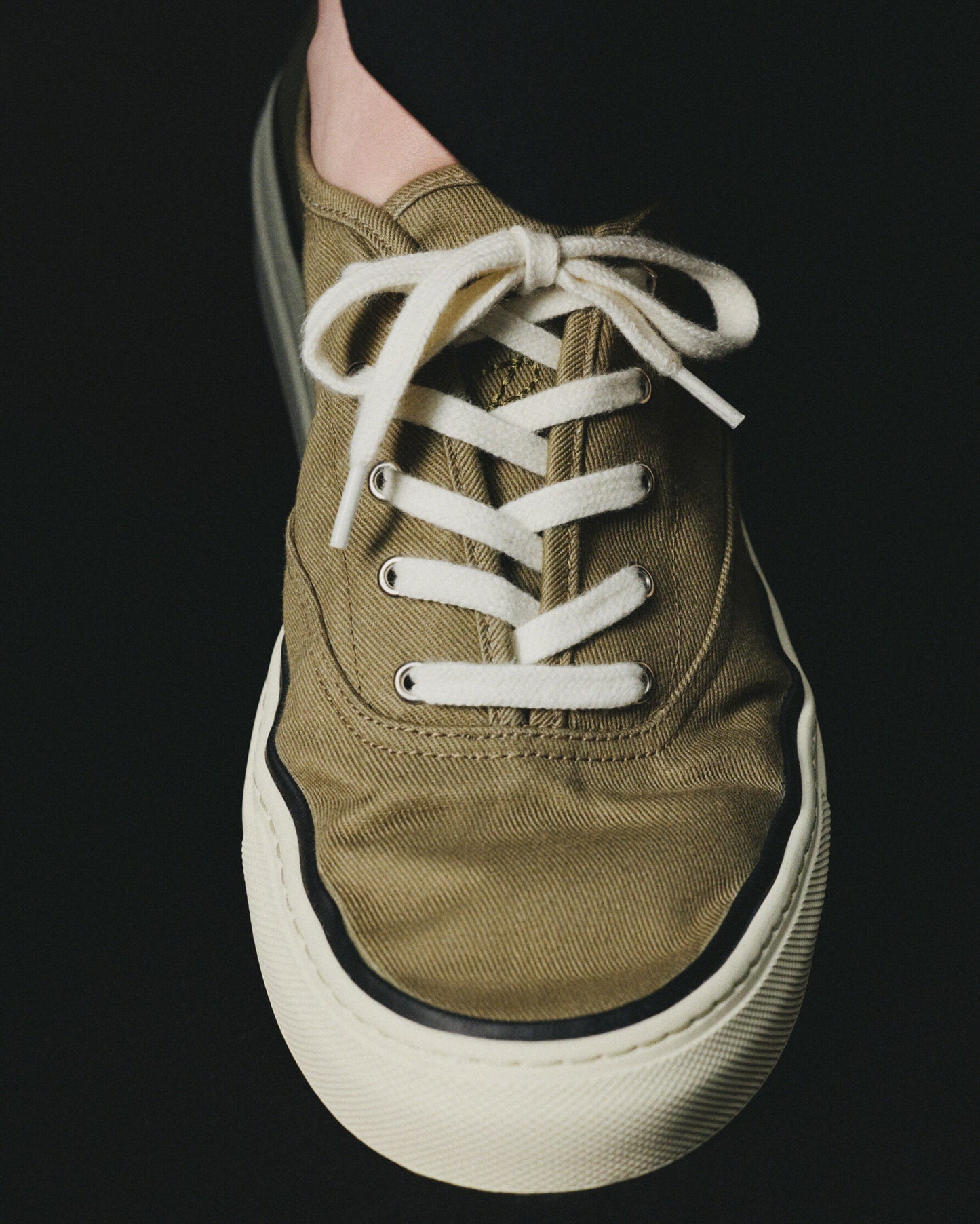 Green sneaker with white laces on a light beige background