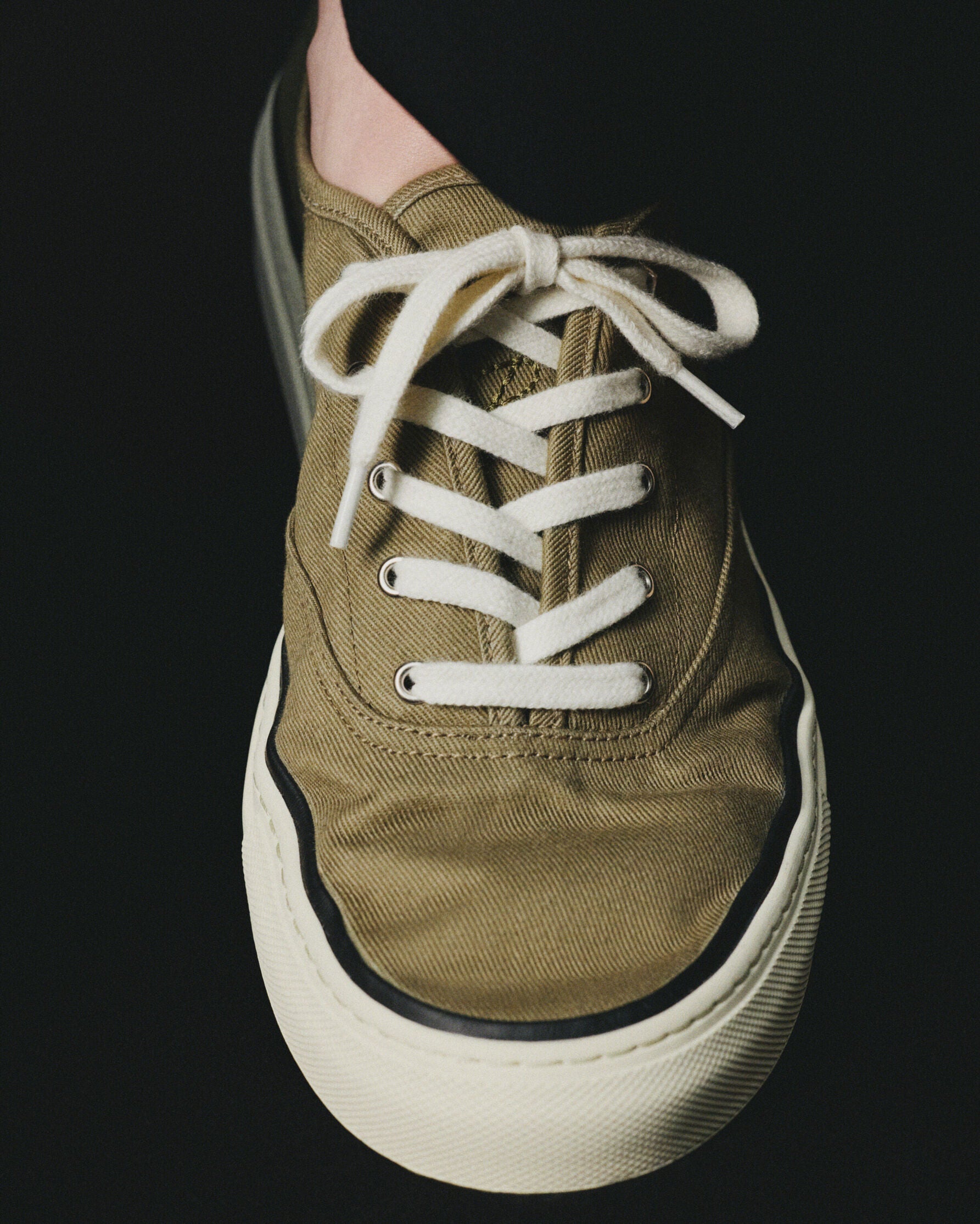 Green sneaker with white laces on a light beige background