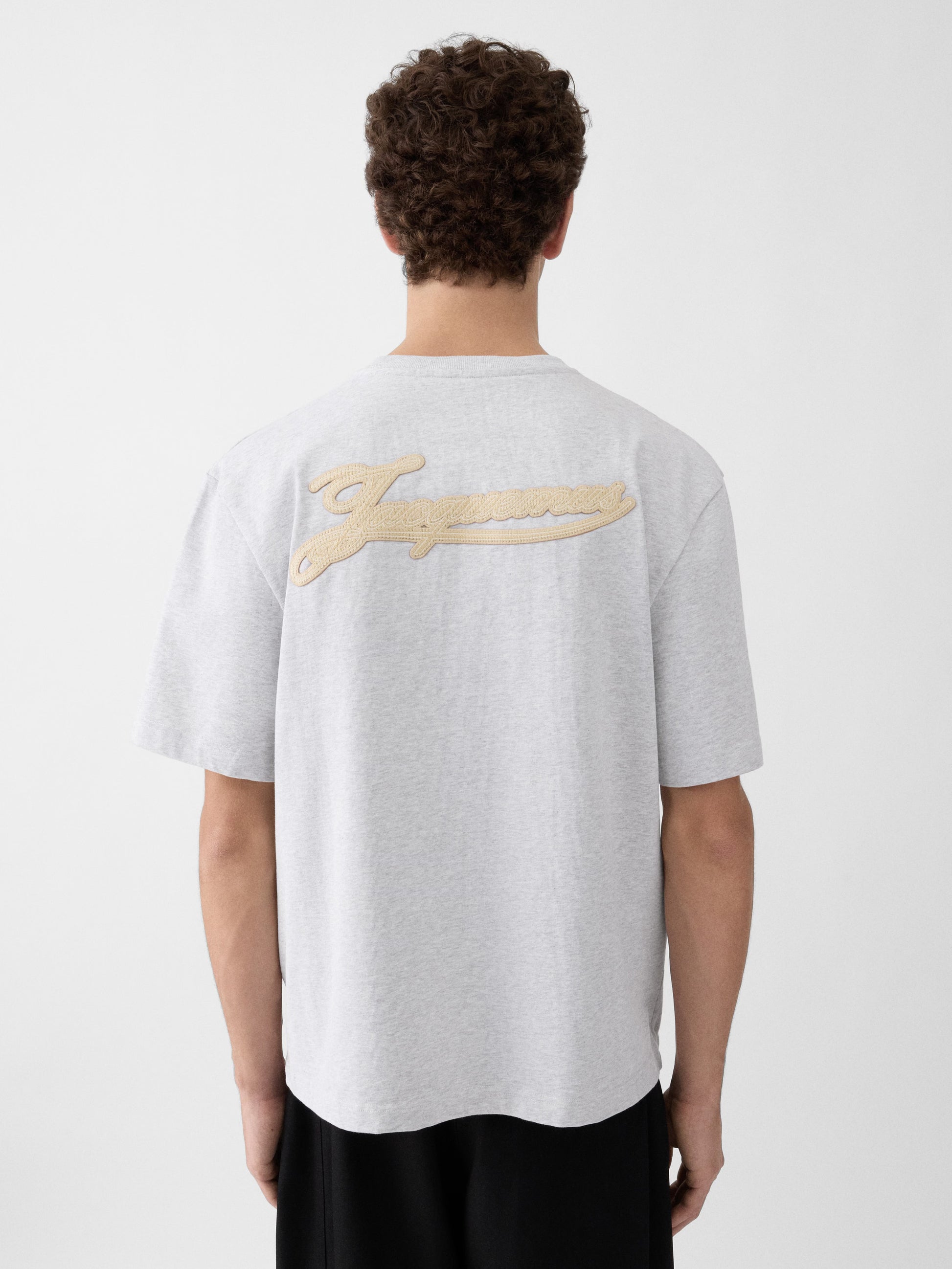 Grey t-shirt with a beige label on a light gray background JACQUEMUS