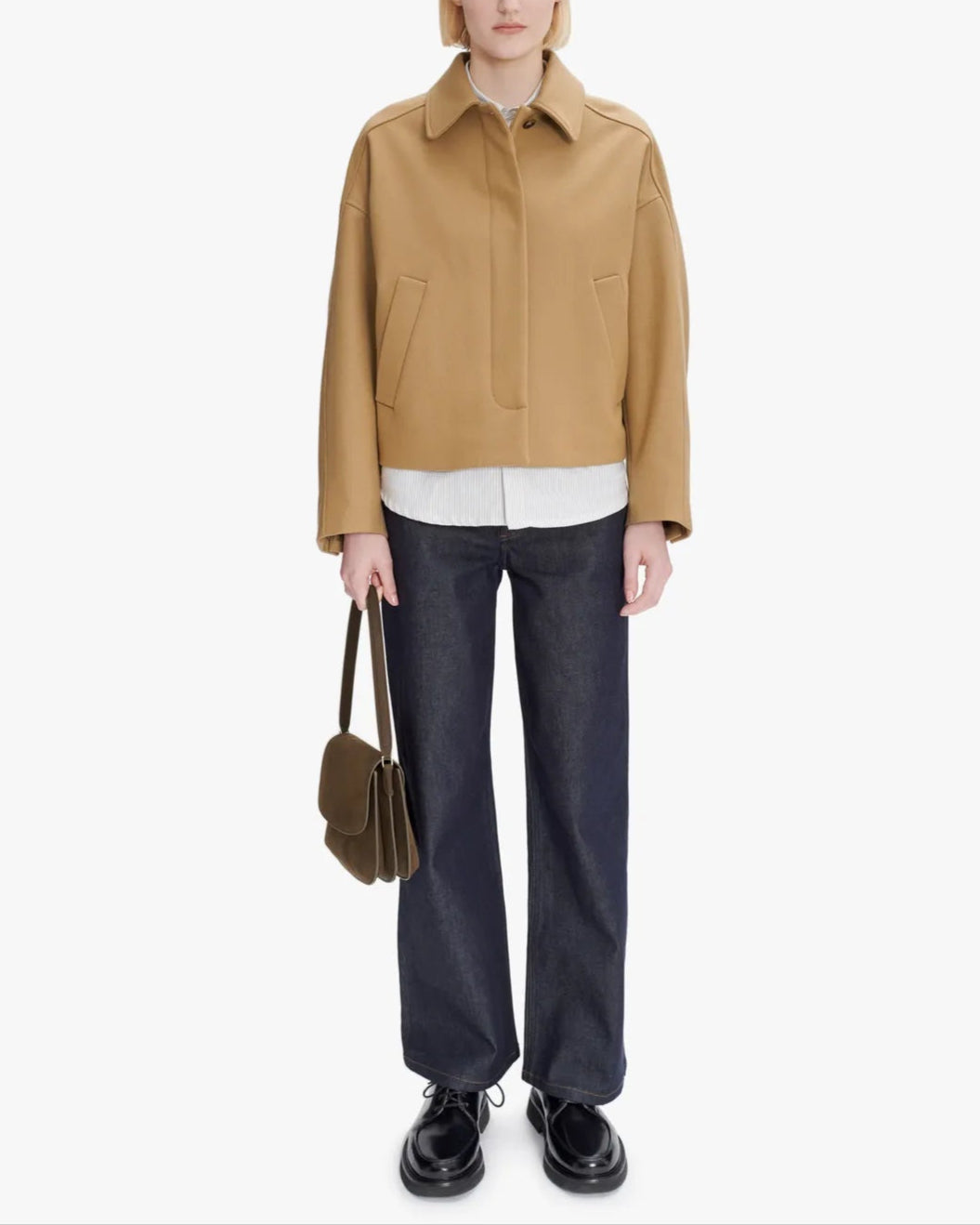 Person wearing a tan jacket, white shirt, dark pants, and black shoes on a white background