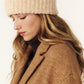 Woman wearing a beige knit beanie and brown coat on a white background