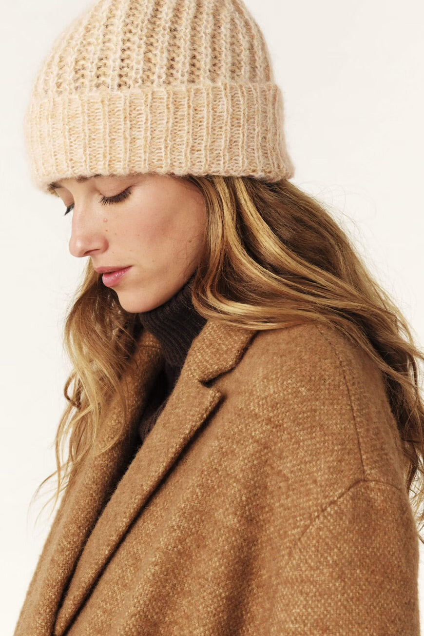 Woman wearing a beige knit beanie and brown coat on a white background