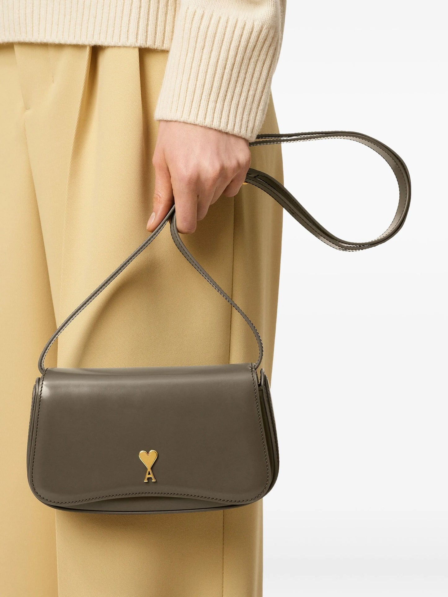 Green handbag with a gold heart emblem on a light beige background ami paris