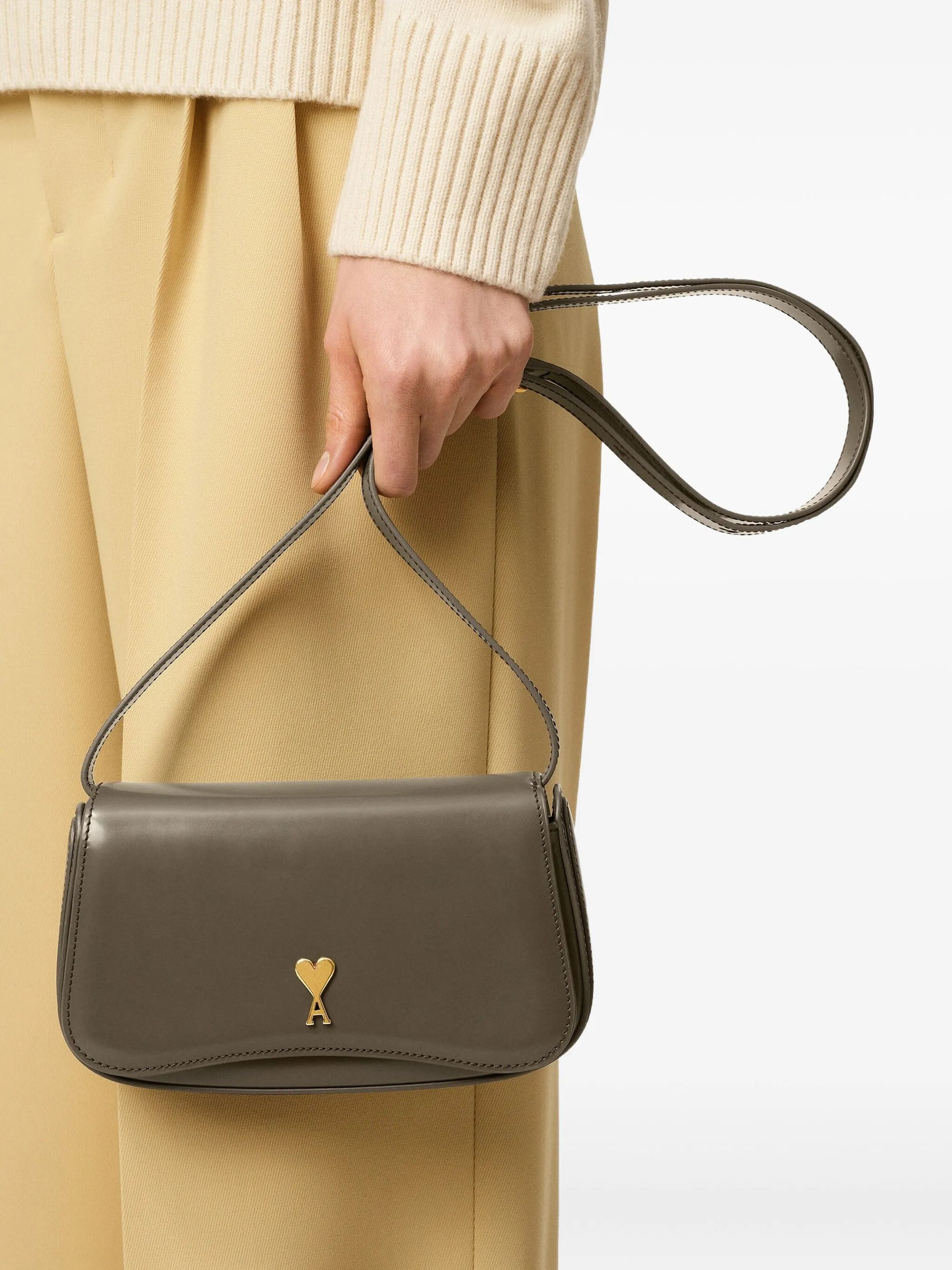 Green handbag with a gold heart emblem on a light beige background ami paris