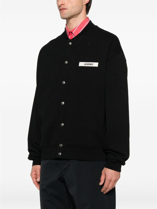 Black varsity jacket with a logo on the chest against a white background