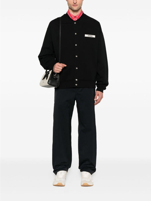 Black varsity jacket with a logo on the chest against a white background