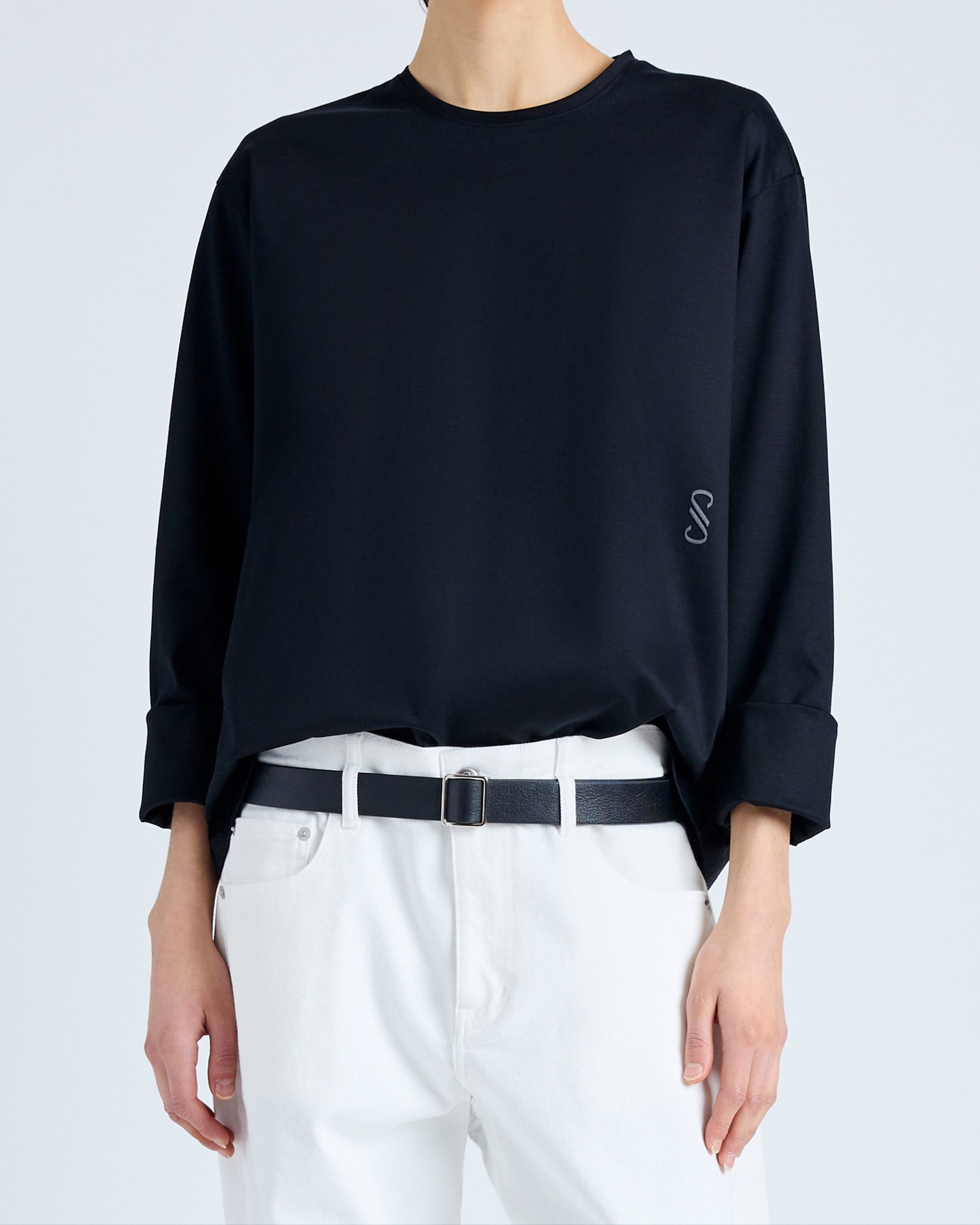 Person wearing a black oversized shirt with a small logo on a light gray background
