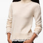 A light beige knit turtleneck sweater with long sleeves and a sheer ruffled hem, displayed against a plain white background.