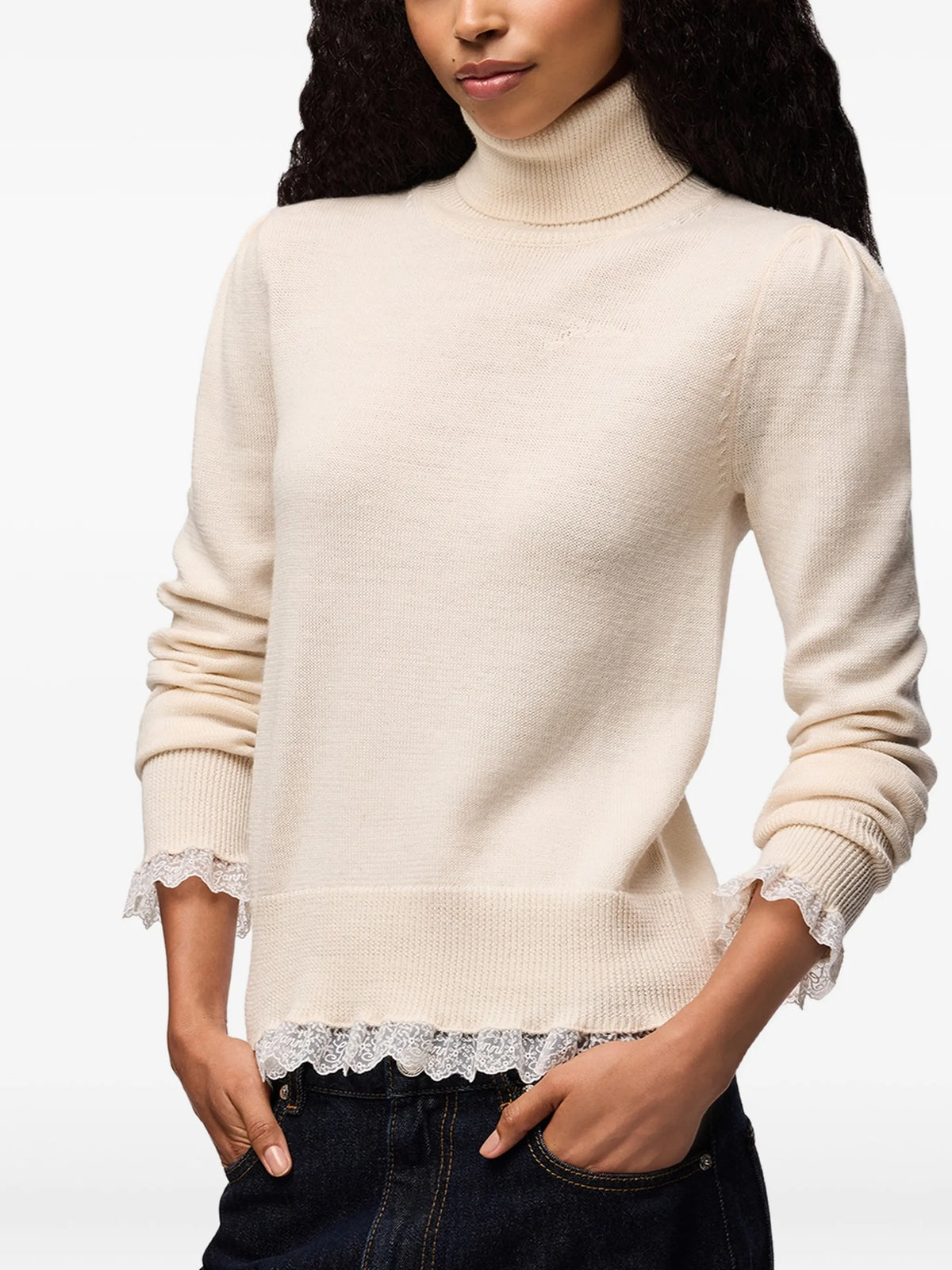 A light beige knit turtleneck sweater with long sleeves and a sheer ruffled hem, displayed against a plain white background.