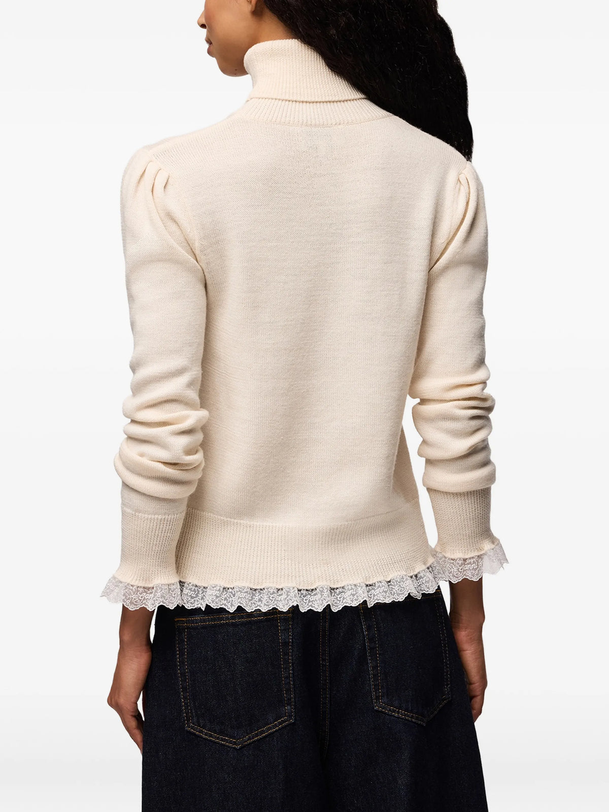 A light beige knit turtleneck sweater with long sleeves and a sheer ruffled hem, displayed against a plain white background.