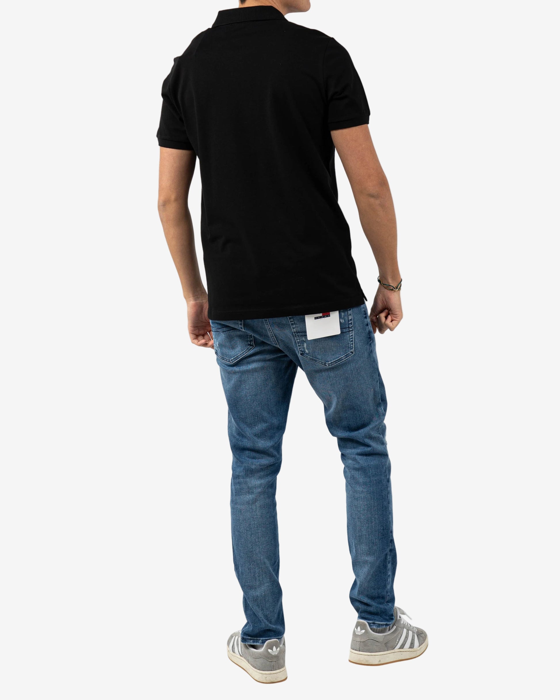Person wearing a black polo shirt and blue jeans on a white background