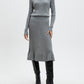 Woman wearing a gray ribbed sweater and skirt set with black knee-high boots on a white background