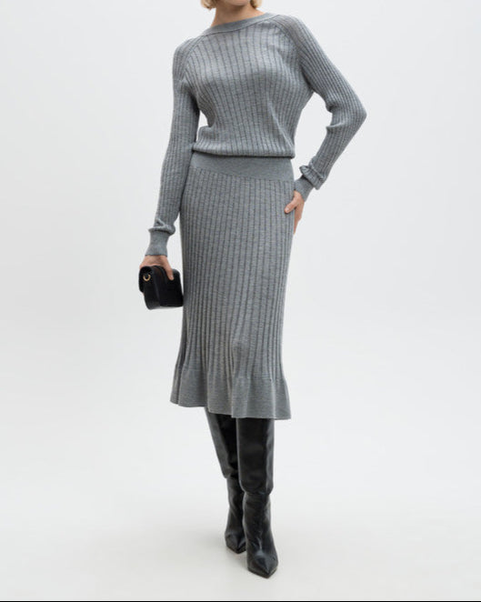 Woman wearing a gray ribbed sweater and skirt set with black knee-high boots on a white background