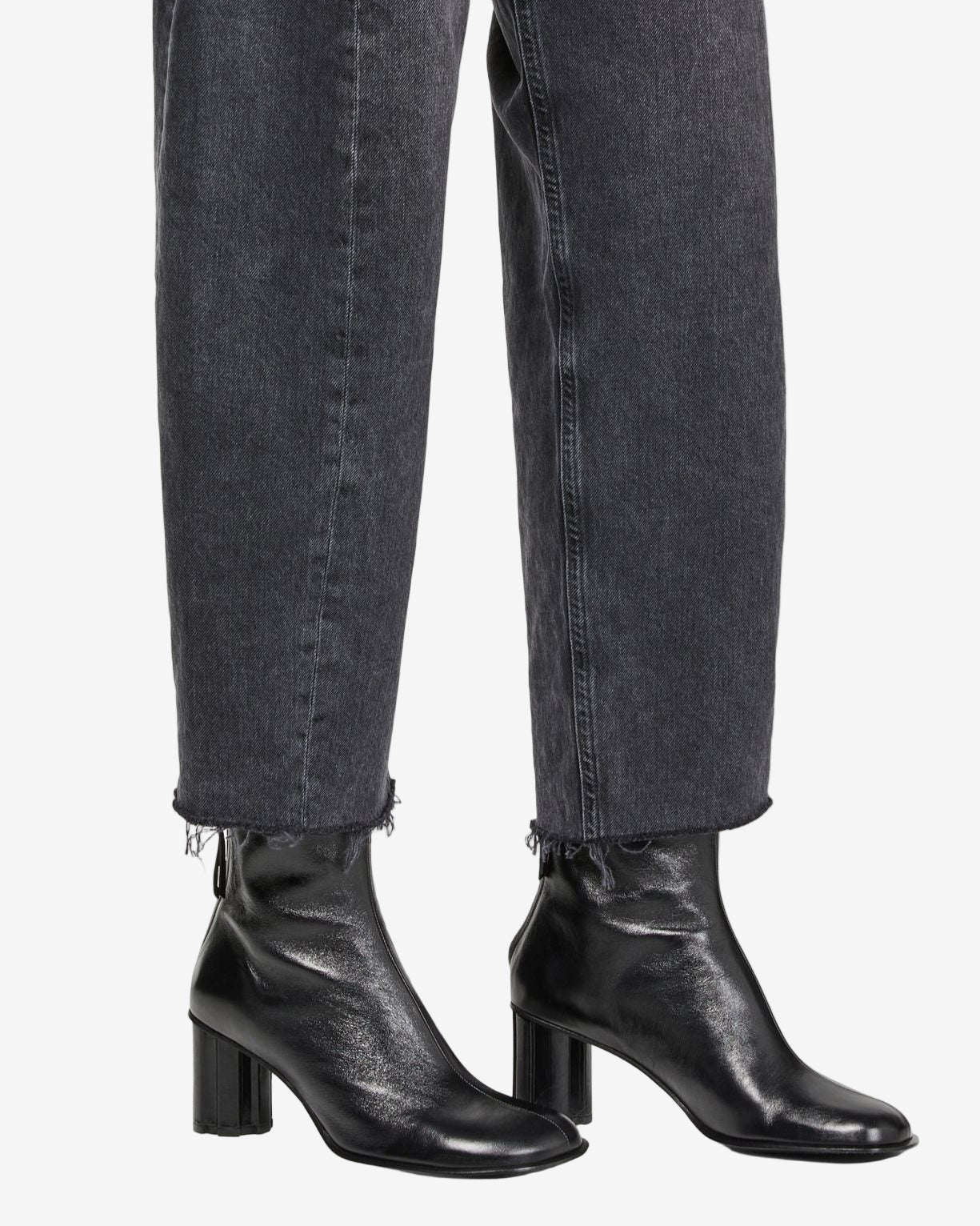 Black leather ankle boots worn with black jeans on a white background