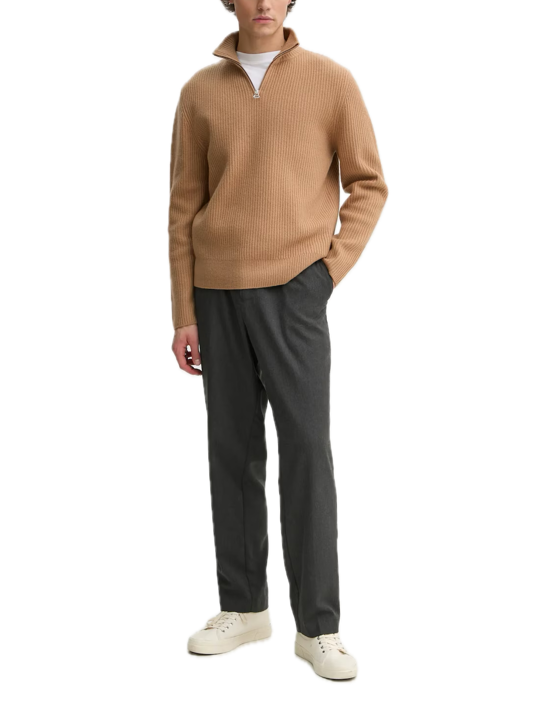 Man wearing a beige sweater and gray pants on a white background