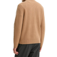 Person wearing a beige ribbed sweater and dark pants on a white background