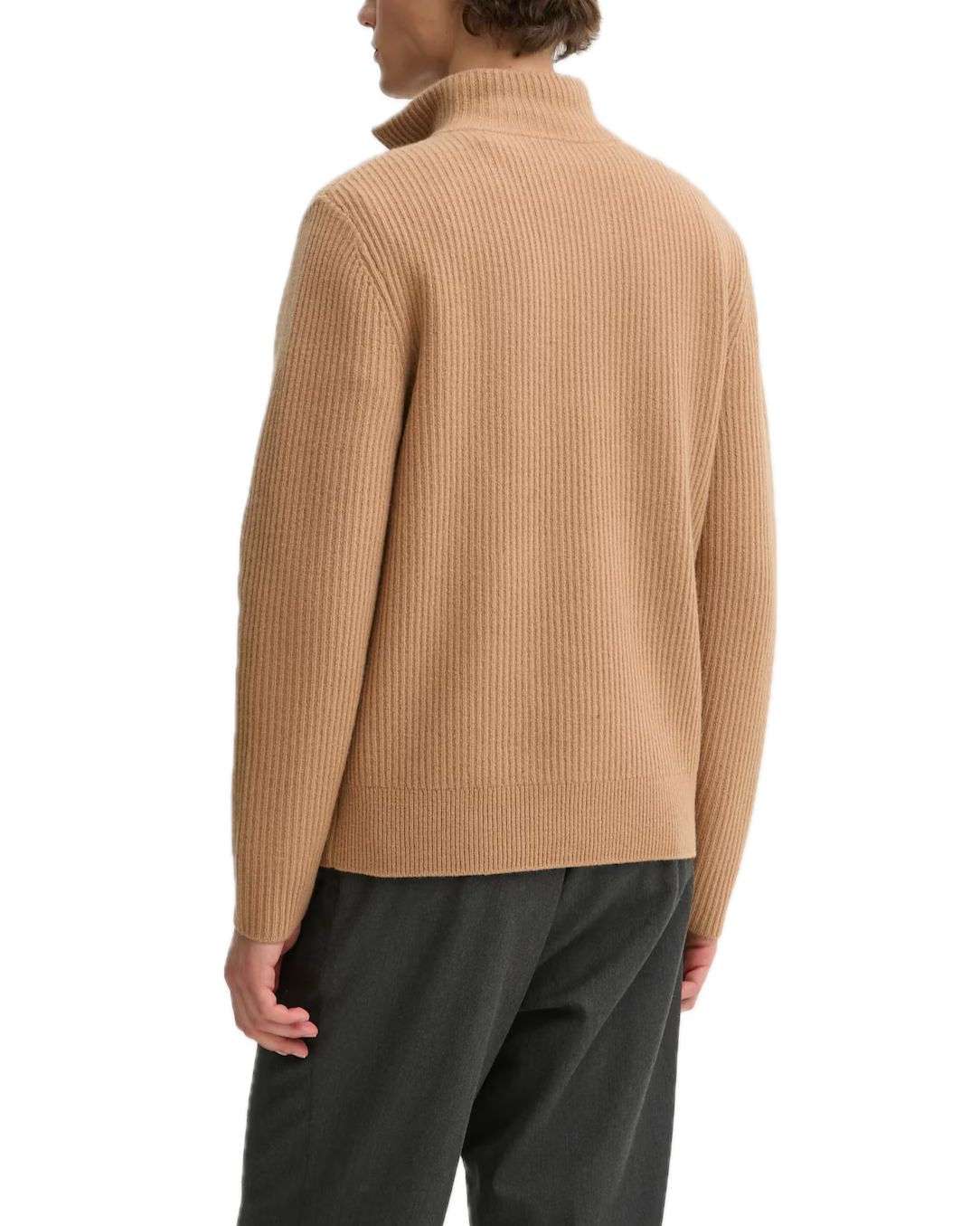 Person wearing a beige ribbed sweater and dark pants on a white background