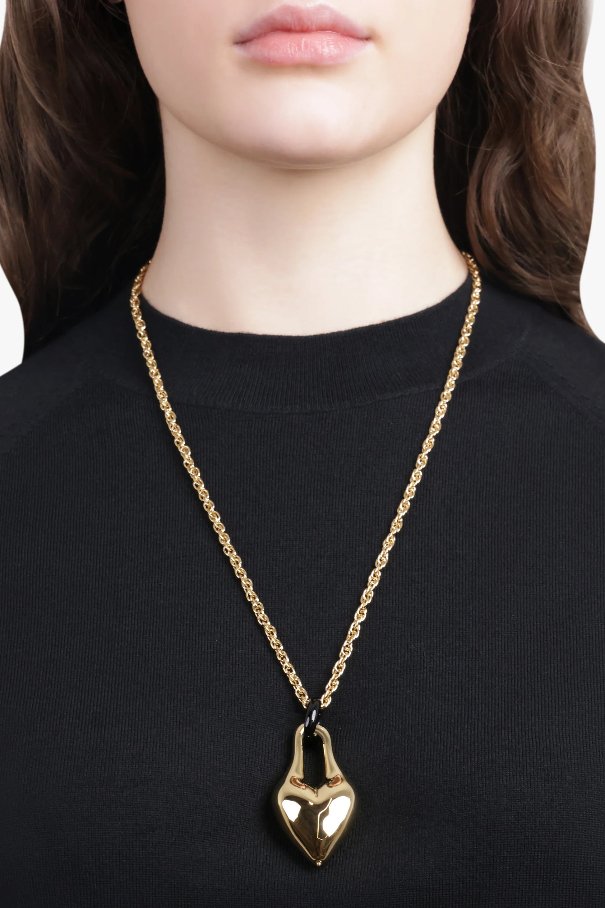 Gold necklace with a heart pendant worn by a person on a black background