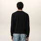 Black sweater with a small red heart emblem on a beige background