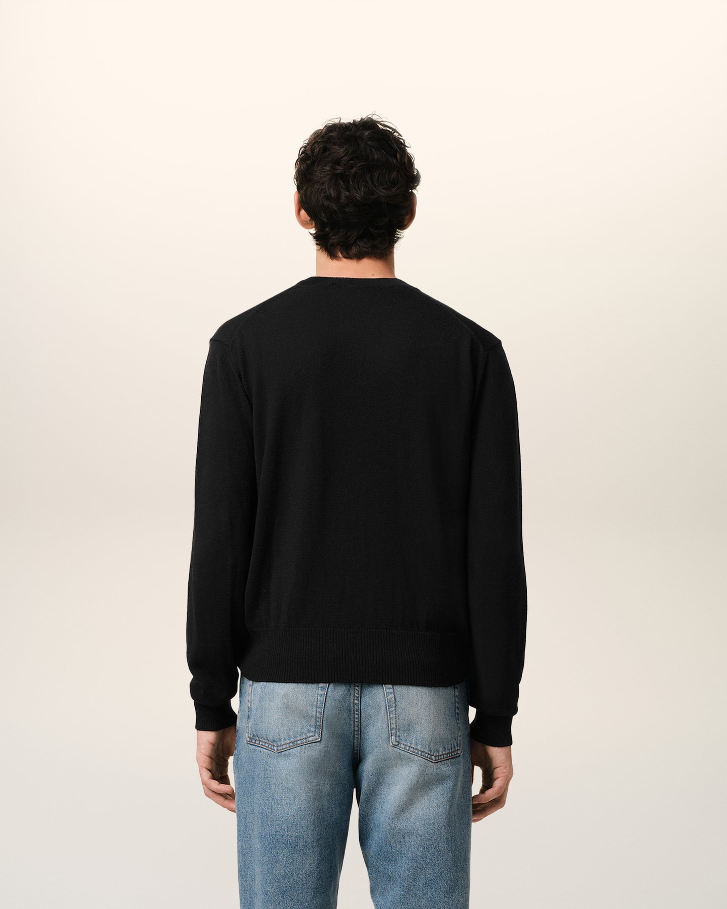 Black sweater with a small red heart emblem on a beige background