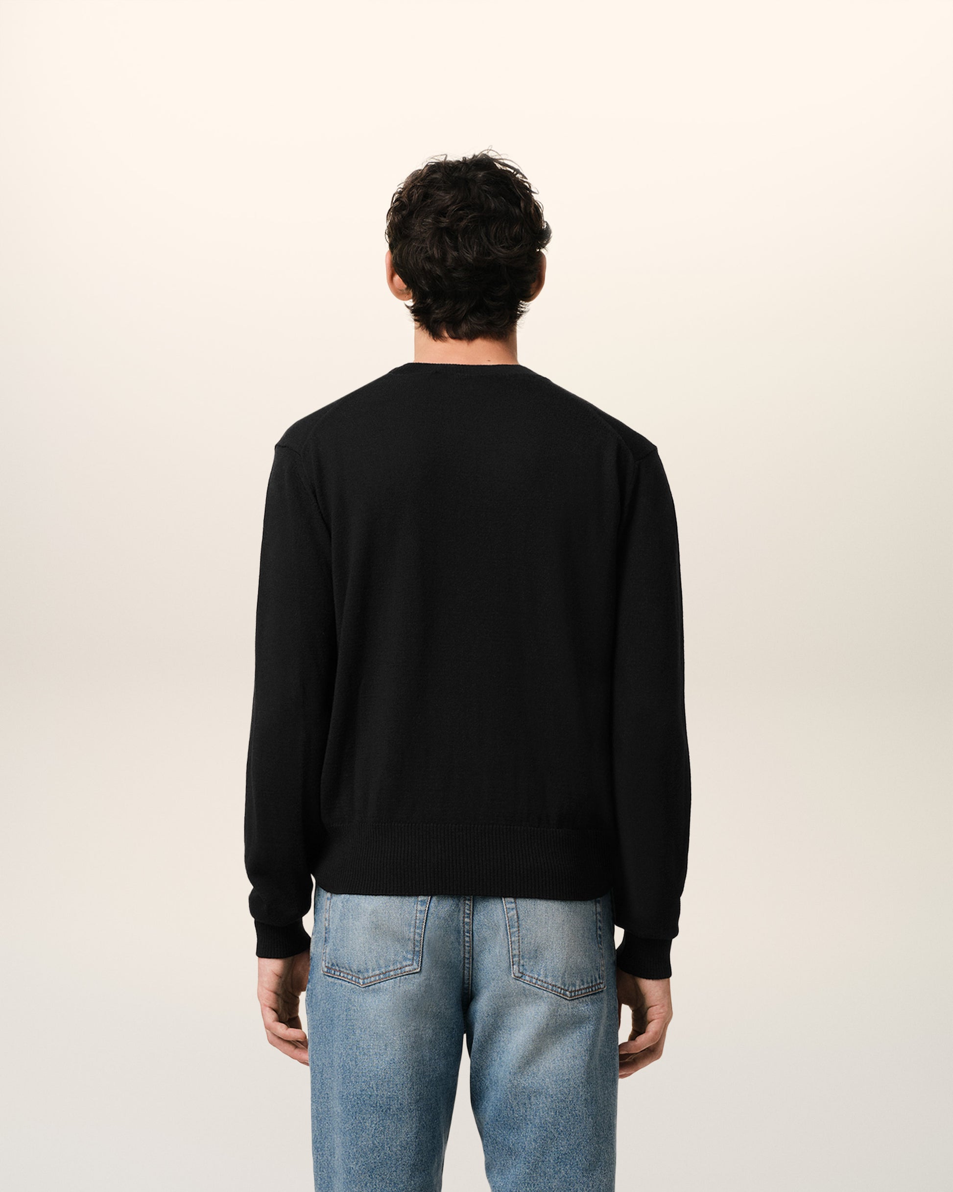 Black sweater with a small red heart emblem on a beige background