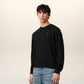 Black sweater with a small red heart emblem on a beige background