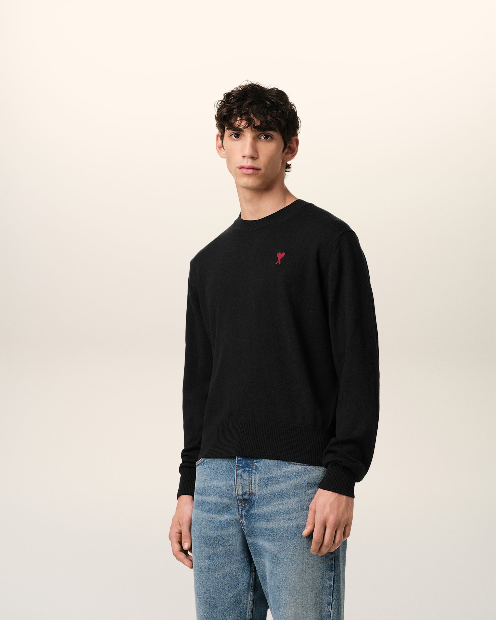 Black sweater with a small red heart emblem on a beige background
