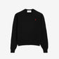 Black sweater with a small red heart emblem on a beige background