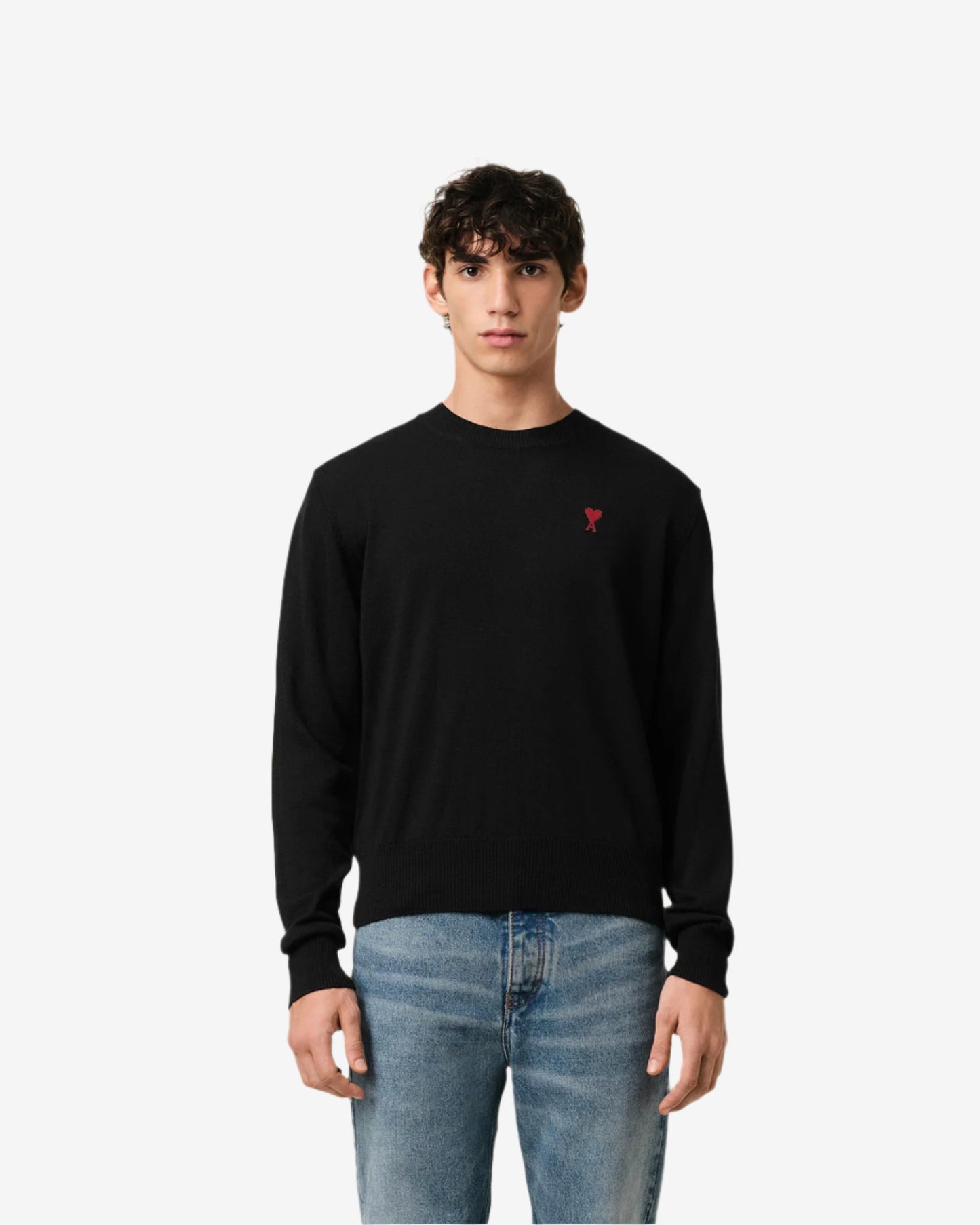 Black sweater with a small red heart emblem on a beige background