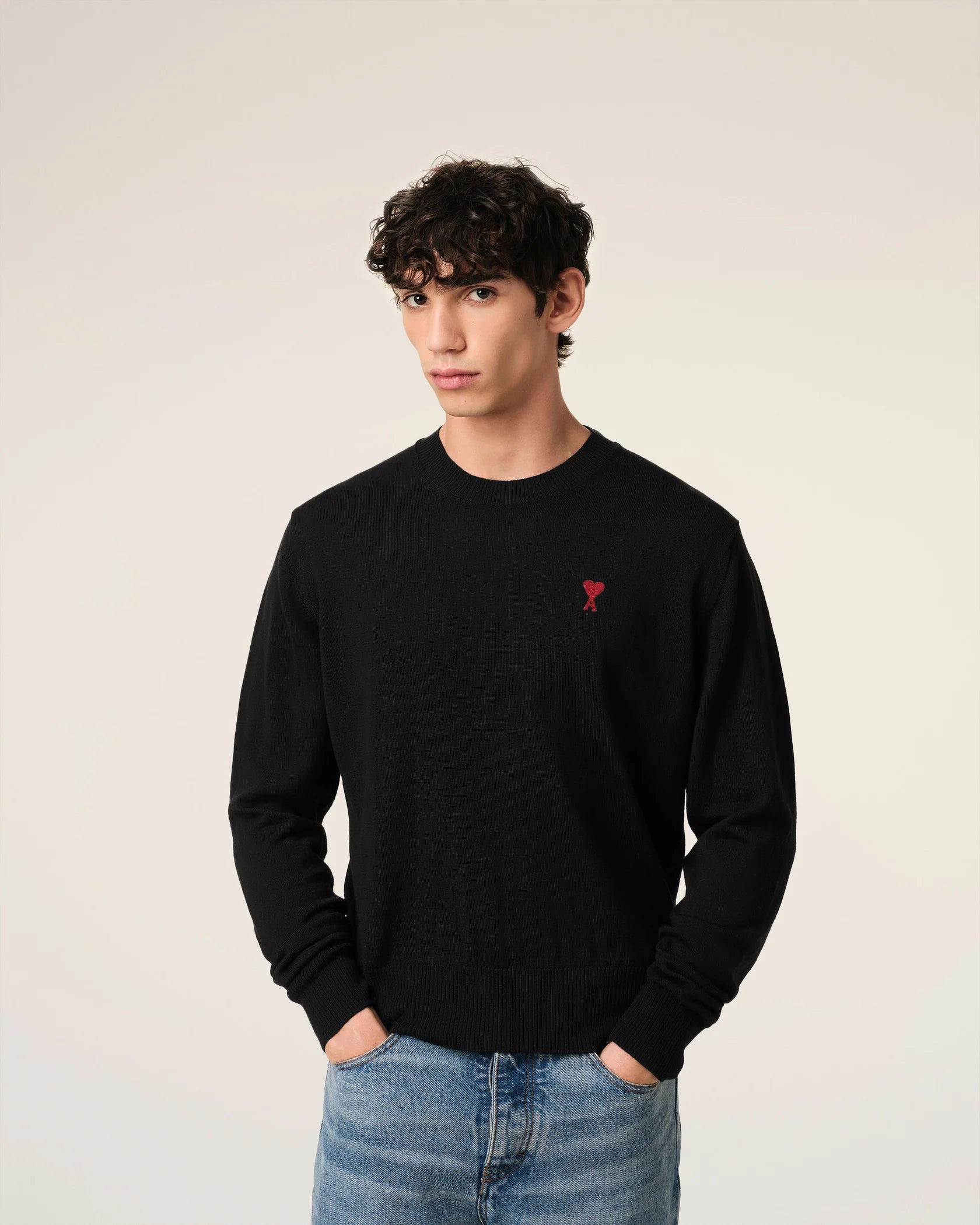 Black sweater with a small red heart emblem on a beige background