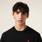 Black sweater with a small red heart emblem on a beige background