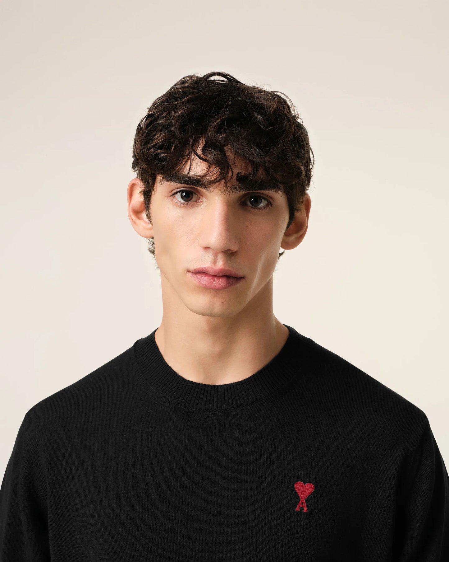 Black sweater with a small red heart emblem on a beige background