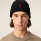 A black ribbed knit beanie hat featuring a small red embroidered heart logo with a letter A on the front cuff, set against a plain off-white background.
