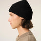 A black ribbed knit beanie hat featuring a small red embroidered heart logo with a letter A on the front cuff, set against a plain off-white background.
