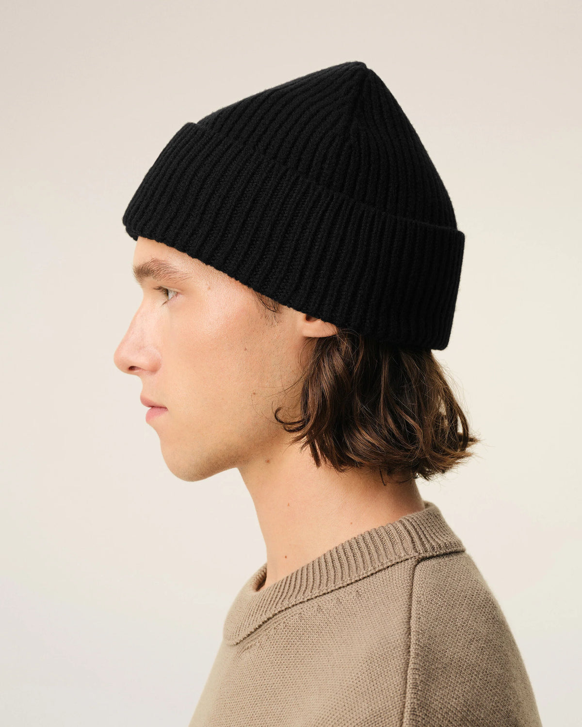 A black ribbed knit beanie hat featuring a small red embroidered heart logo with a letter A on the front cuff, set against a plain off-white background.