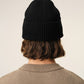 A black ribbed knit beanie hat featuring a small red embroidered heart logo with a letter A on the front cuff, set against a plain off-white background.