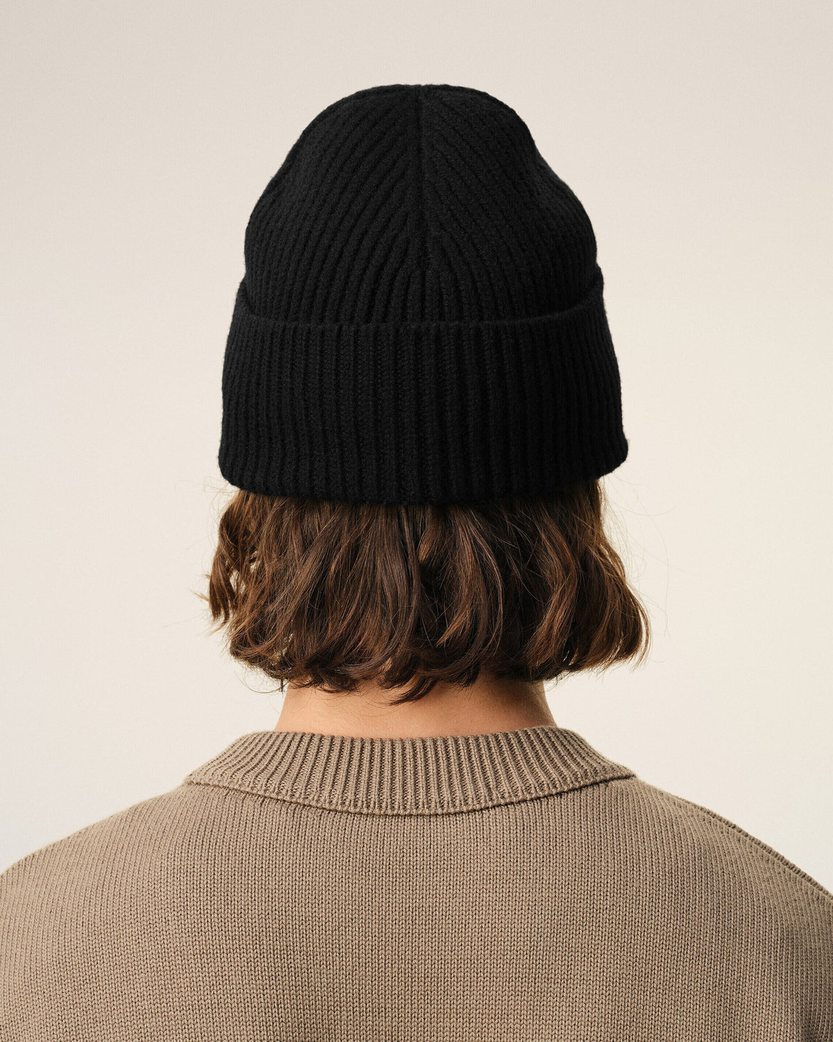 A black ribbed knit beanie hat featuring a small red embroidered heart logo with a letter A on the front cuff, set against a plain off-white background.