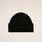 A black ribbed knit beanie hat featuring a small red embroidered heart logo with a letter A on the front cuff, set against a plain off-white background.