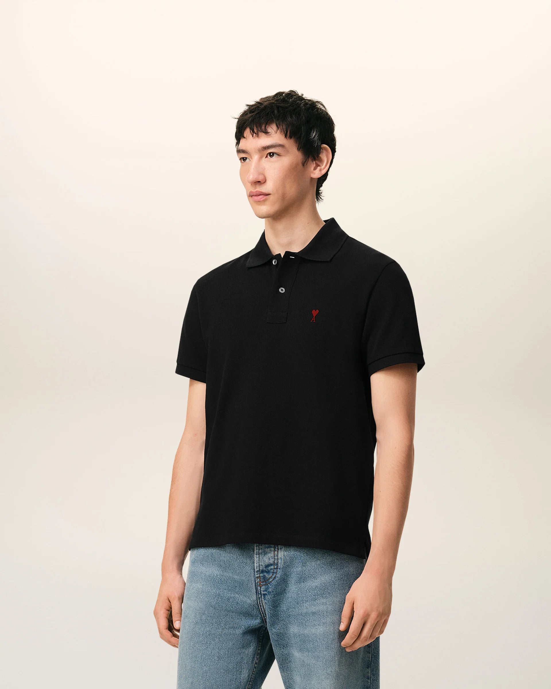 Black polo shirt with a red heart emblem on a beige background ami paris