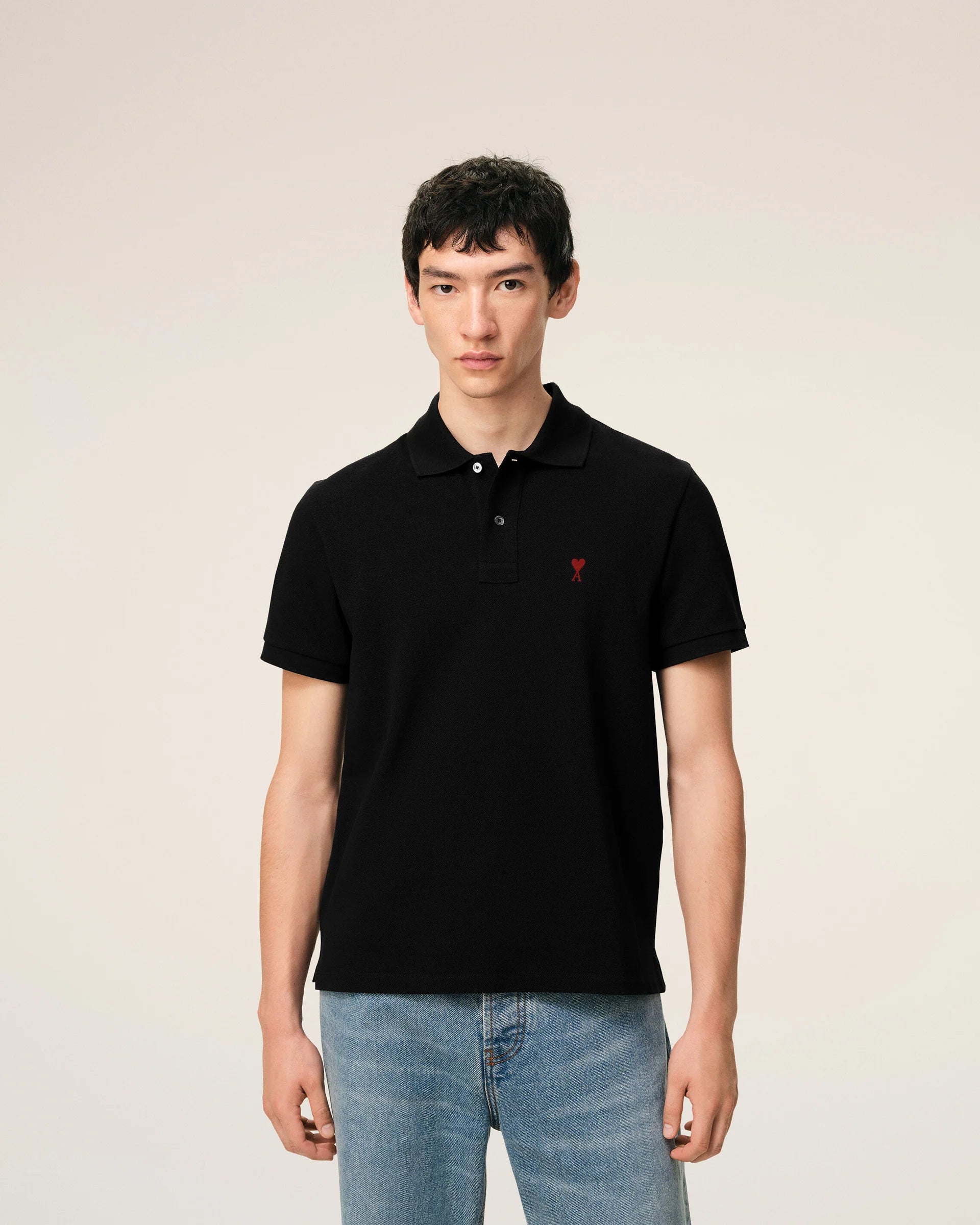 Black polo shirt with a red heart emblem on a beige background ami paris