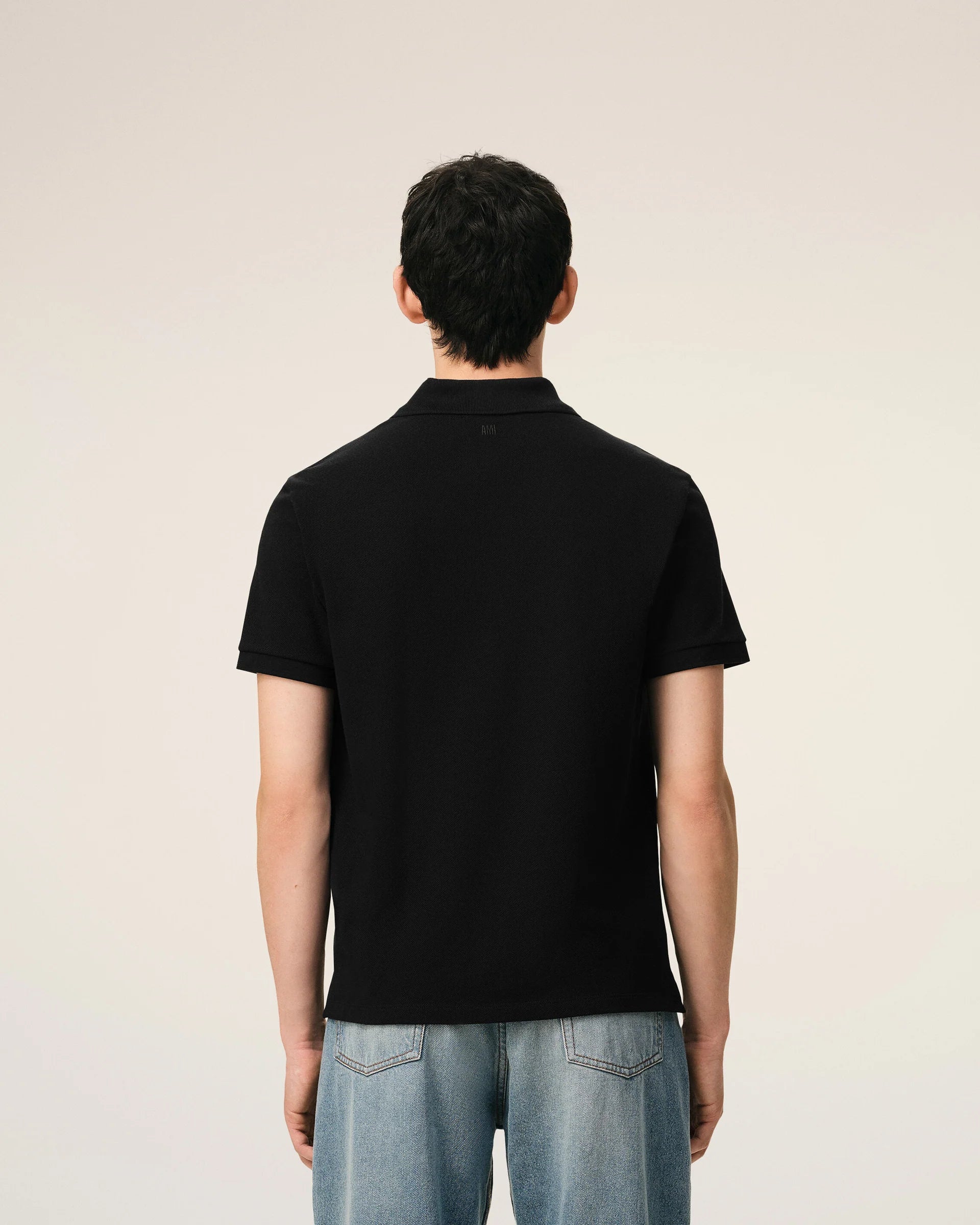 Black polo shirt with a red heart emblem on a beige background ami paris